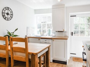 A modern kitchen with white cabinetry, a wooden dining table, and a black wall clock.