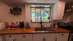 Une cuisine dotée d’un plan de travail en bois, de meubles blancs, d’une fenêtre donnant sur un espace verdoyant et de divers appareils de cuisine.