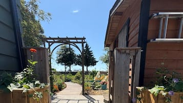 A wooden entrance gate with a pathway leading to a garden area, surrounded by wooden fences and plants.