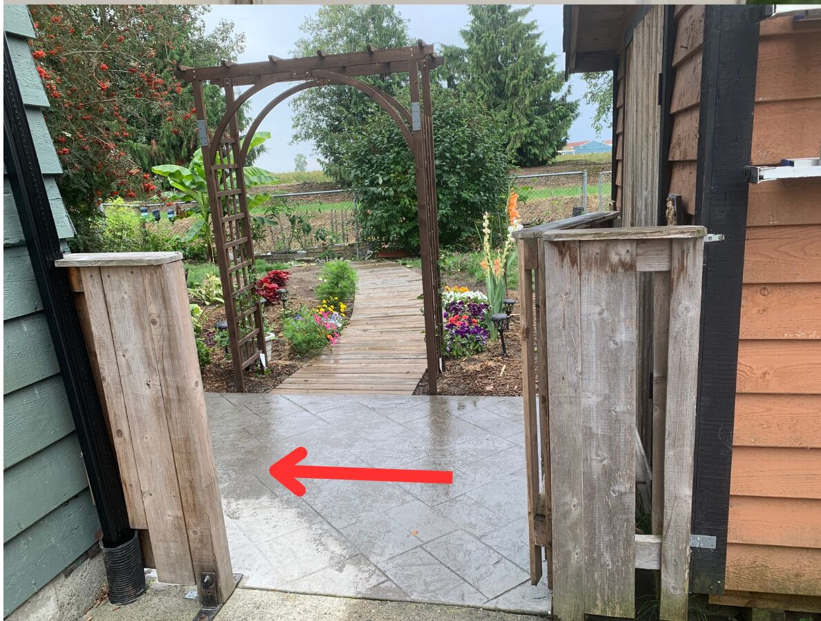 A wooden pergola entrance to a garden with a pathway leading through it.