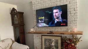 Un salon avec un téléviseur fixé au mur en briques, un meuble en bois, un canapé, une cheminée et un vase de fleurs.