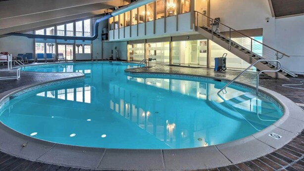 An indoor swimming pool with a central staircase and a view of the adjacent building.