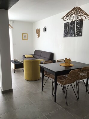 Ein modernes Wohnzimmer mit grauem Sofa, gelbem Ottomanen und einem Esstisch mit Korbstühlen.