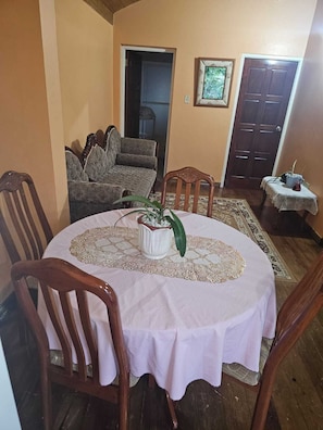 Un coin repas avec une table ronde, des chaises, une plante en pot et une porte en arrière-plan.
