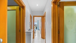 A hallway with wooden doors, a white tiled floor, and a view of a balcony with a blue curtain.