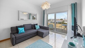 A modern living room with a grey sofa, a large mirror, and a balcony with a view of the city.