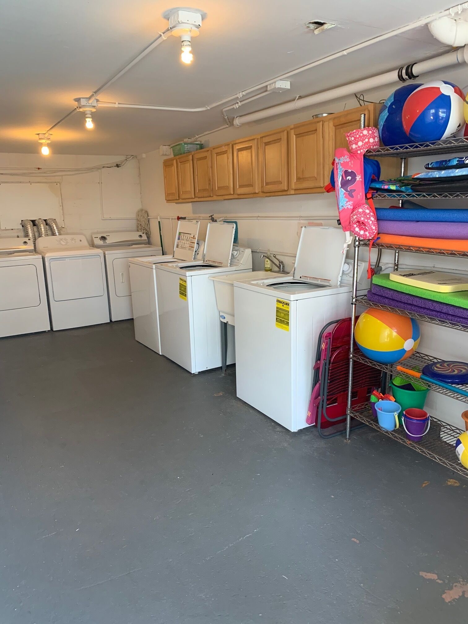 A laundry room with multiple washing machines, wooden cabinets, and a shelf with colorful beach balls.
