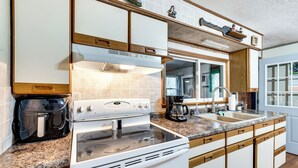 Una cocina con armarios blancos, estufa, cafetera y lavabo.
