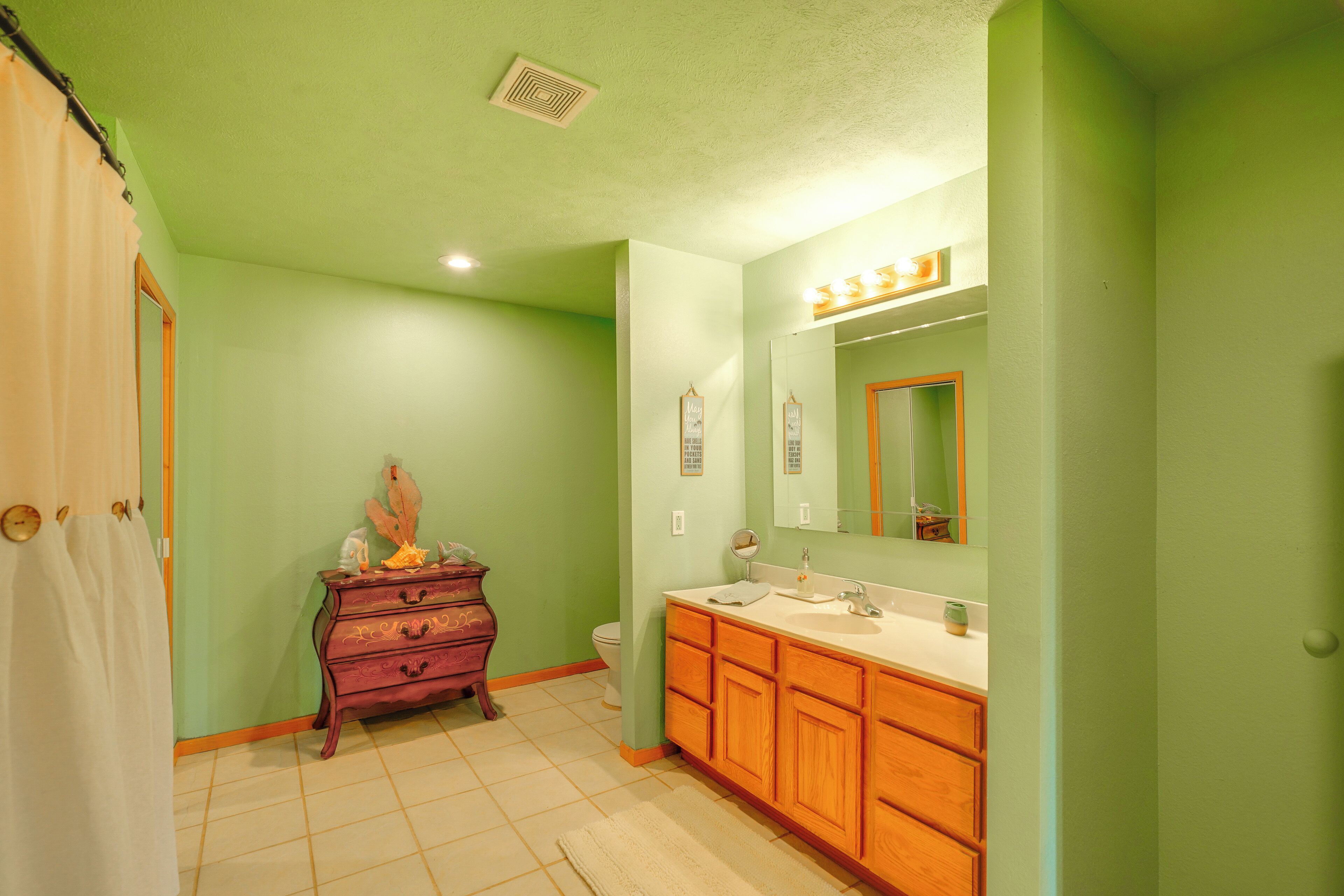 A bathroom with green walls, a wooden vanity, a mirror, and a toilet.