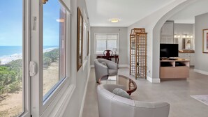 Amplia sala de estar con un gran ventanal con vista a la playa, un espacio de estar cómodo y un mueble moderno para entretenimiento.