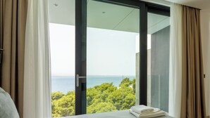 A bedroom with a large window, a bed, and a view of the sea and trees. - Villa Brela-Rogac1 (Brela)