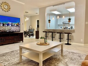 Una sala de estar moderna con un televisor de pantalla plana grande, una mesa de centro blanca y un tapete estampado.