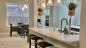 A modern kitchen with a central island, bar stools, pendant lights, and hanging plants. - A spacious vacation home for your Family (Helotes)