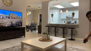 A modern living room with a flat-screen TV, a dining area, and a kitchen visible through an archway. - A spacious vacation home for your Family (Helotes)