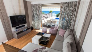 Uma sala de estar moderna com uma grande televisão de tela plana, um sofá, uma mesa de centro e uma varanda com área de estar externa.
