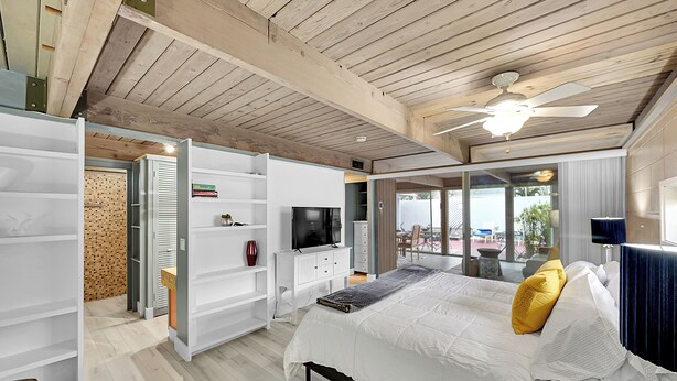 Un dormitorio con cama, televisor, ventilador de techo y vista al exterior.