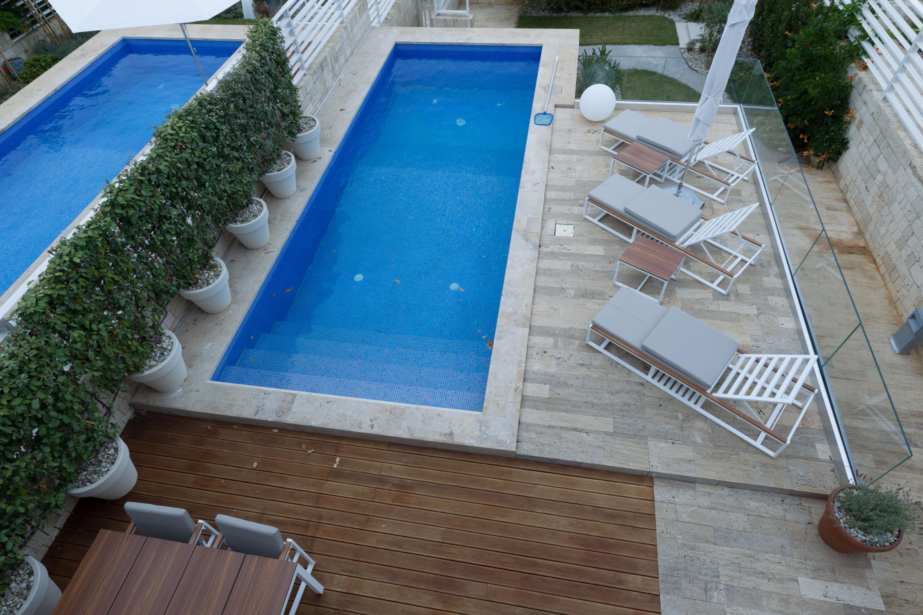 Una piscina rectangular con terraza de madera y sillas de descanso.