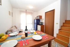 Un coin repas avec une table dressée pour deux personnes, une bouteille de vin et un panier de fruits.
