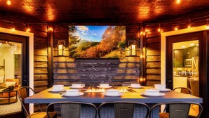Un comedor con una mesa larga dispuesta para cuatro personas, rodeada de sillas, con una chimenea en el centro y un mural panorámico en la pared de fondo.