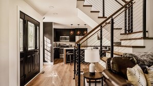 Un interior moderno con una escalera, una zona de cocina y un espacio de estar con una lámpara y cojines.