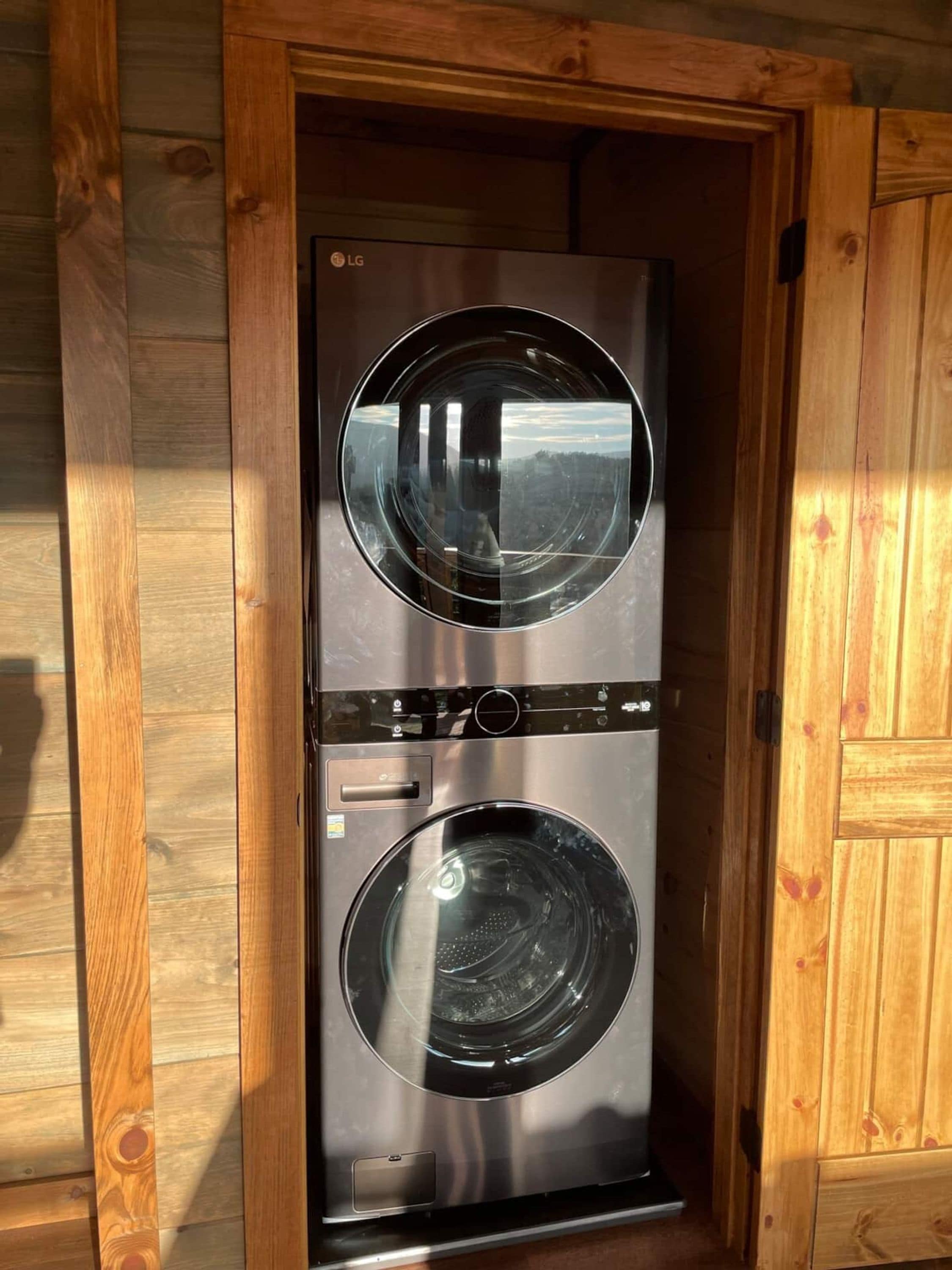 A compact, two-door laundry room with stainless steel appliances, enclosed by wooden paneling.