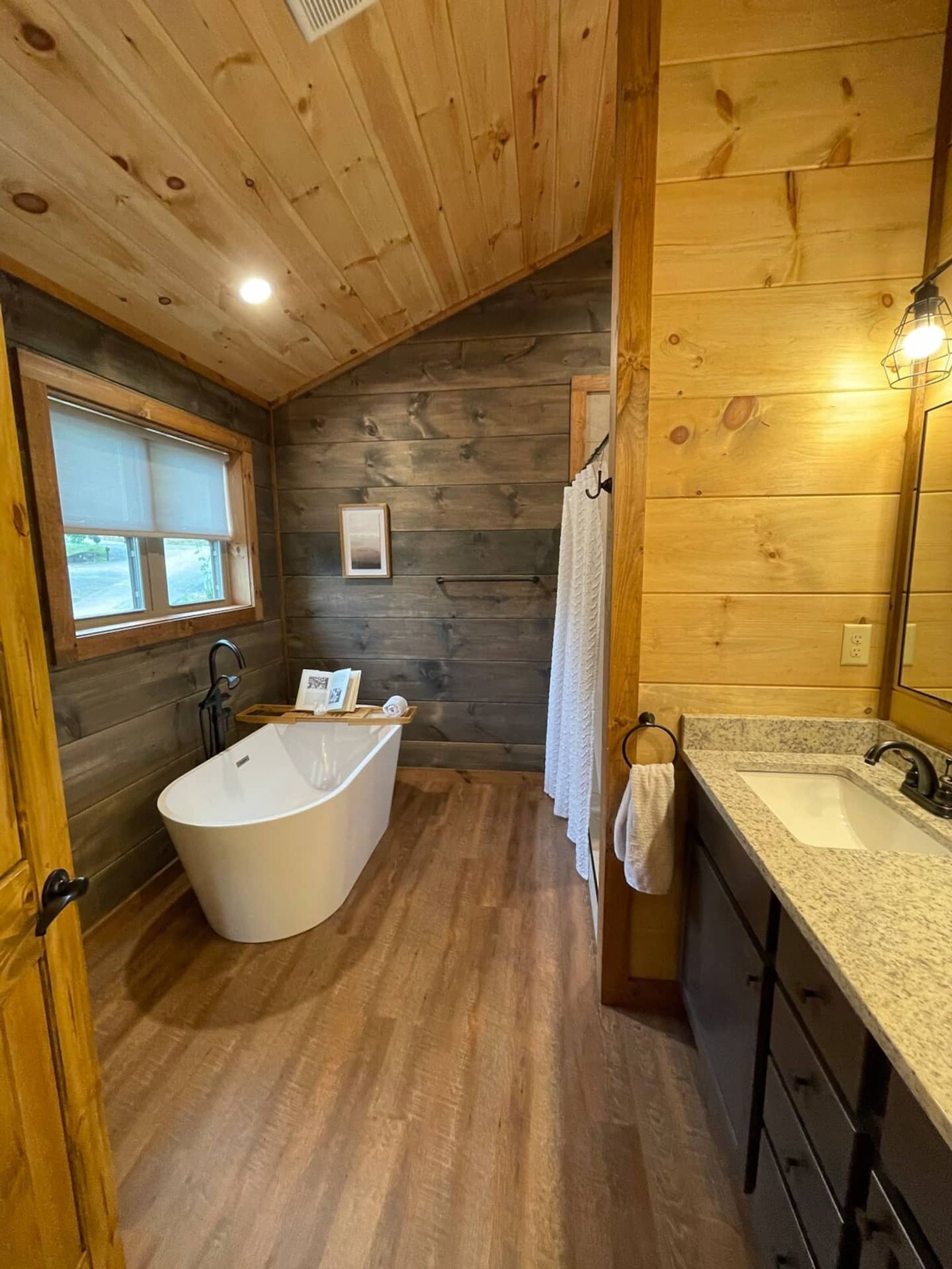 Ein Badezimmer einer Holzhütte mit einer freistehenden Badewanne, einem Waschbecken und einem Fenster.