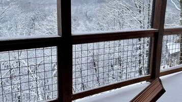 A wooden bench on a snow-covered deck with a view of snow-covered trees and mountains.