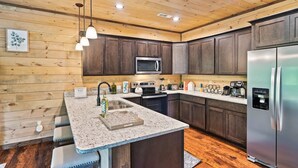 Una cocina moderna con armarios de madera, encimera de granito, electrodomésticos de acero inoxidable e iluminación colgante.