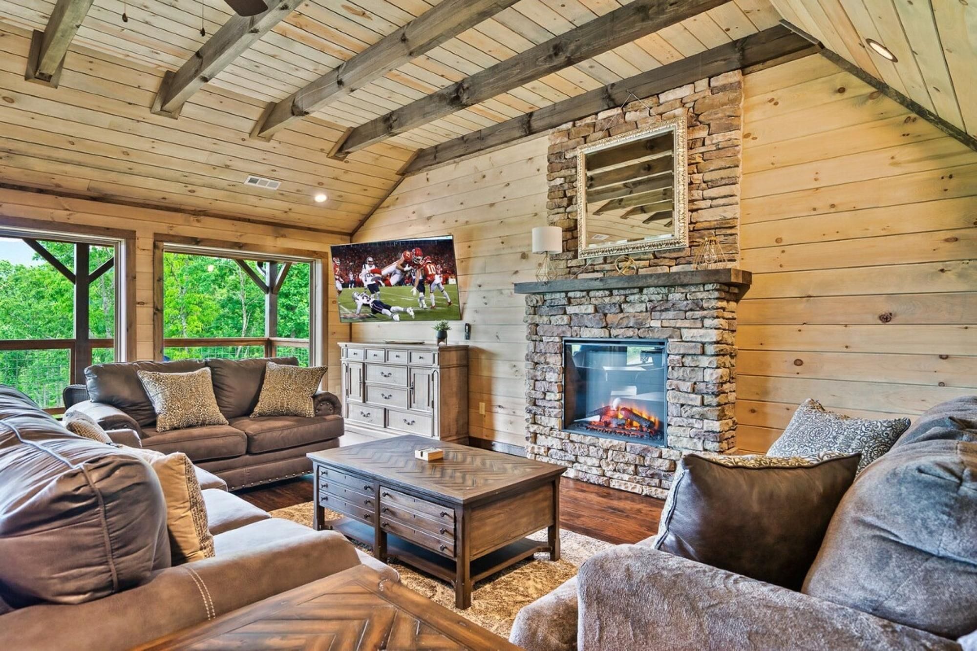 A cozy living room with a stone fireplace, leather sofas, and a television mounted on the wall.