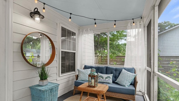 A covered porch with a blue sofa, wicker furniture, a mirror, and string lights. - Frog Cottage (Beaufort)