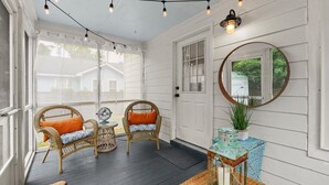 A porch with wicker chairs, a small table, string lights, a fan, a mirror, and a lantern. - Frog Cottage (Beaufort)