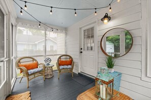 A porch with wicker chairs, a small table, string lights, a fan, a mirror, and a lantern.