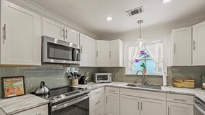 A modern kitchen with white cabinets, stainless steel appliances, a microwave, a kettle, and a toaster. - Frog Cottage (Beaufort)
