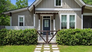 Une maison à deux étages avec un porche à l’avant, une entrée fermée par un portail et une pelouse bien entretenue.
