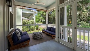 Un porche abrité avec un ventilateur de plafond, deux canapés avec des coussins et un pouf à motifs.