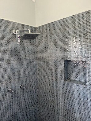 A shower area with a tiled wall, a showerhead, and a shelf.