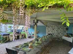 An outdoor dining area with a long wooden table set for a meal, surrounded by greenery and a white building in the background. - Le Manoir Lacustre Medoc, large house near castles and Ocean15 to 22 people (Queyrac)