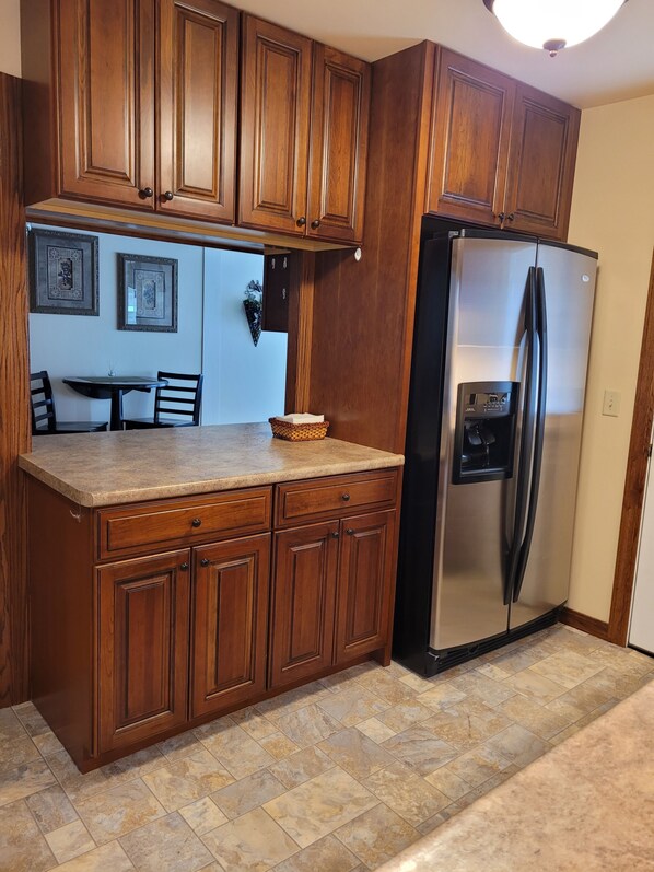 Una cocina con armarios de madera, un refrigerador de acero inoxidable, encimera de granito y un comedor con sillas y una mesa.