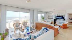 Un salón amplio con balcón, muebles blancos y televisor.