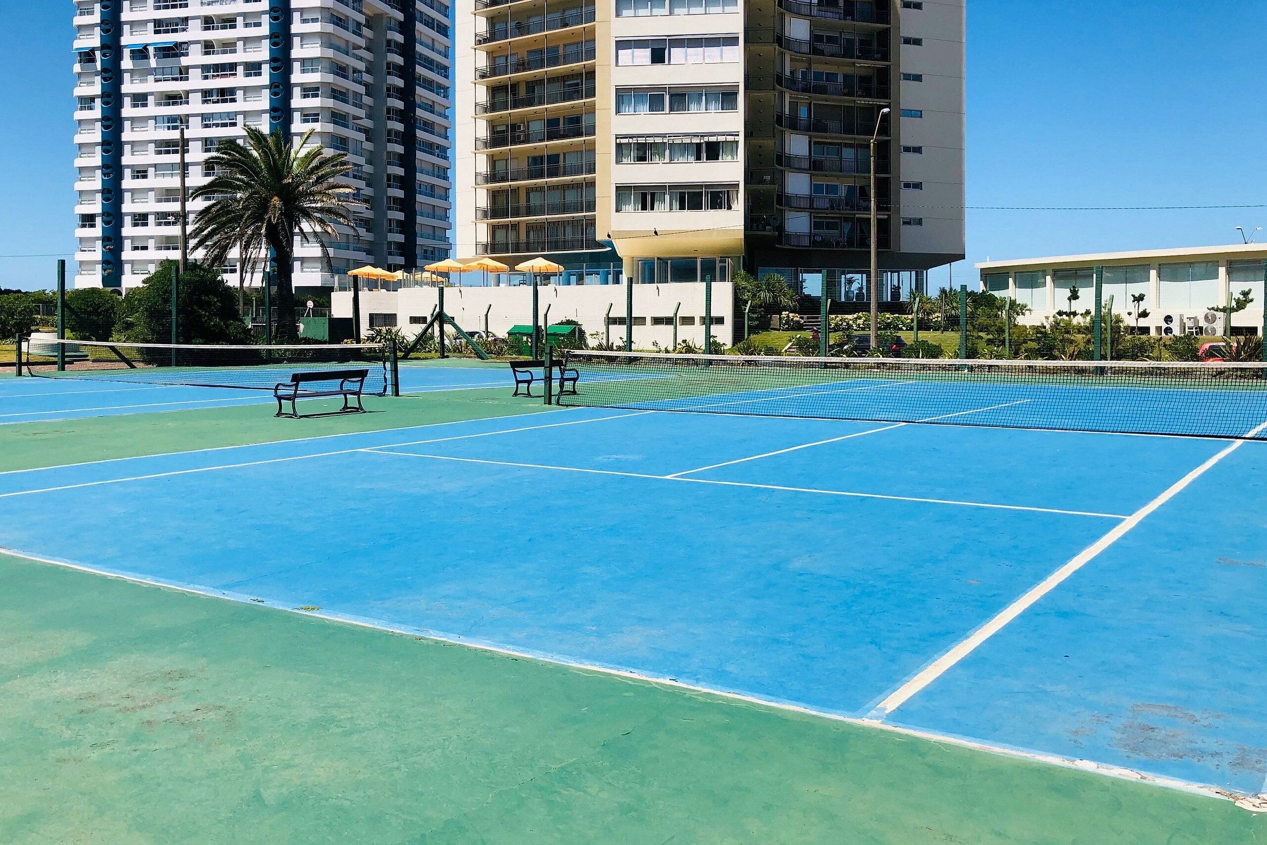 Una cancha de tenis con red, bancos y sombrillas.