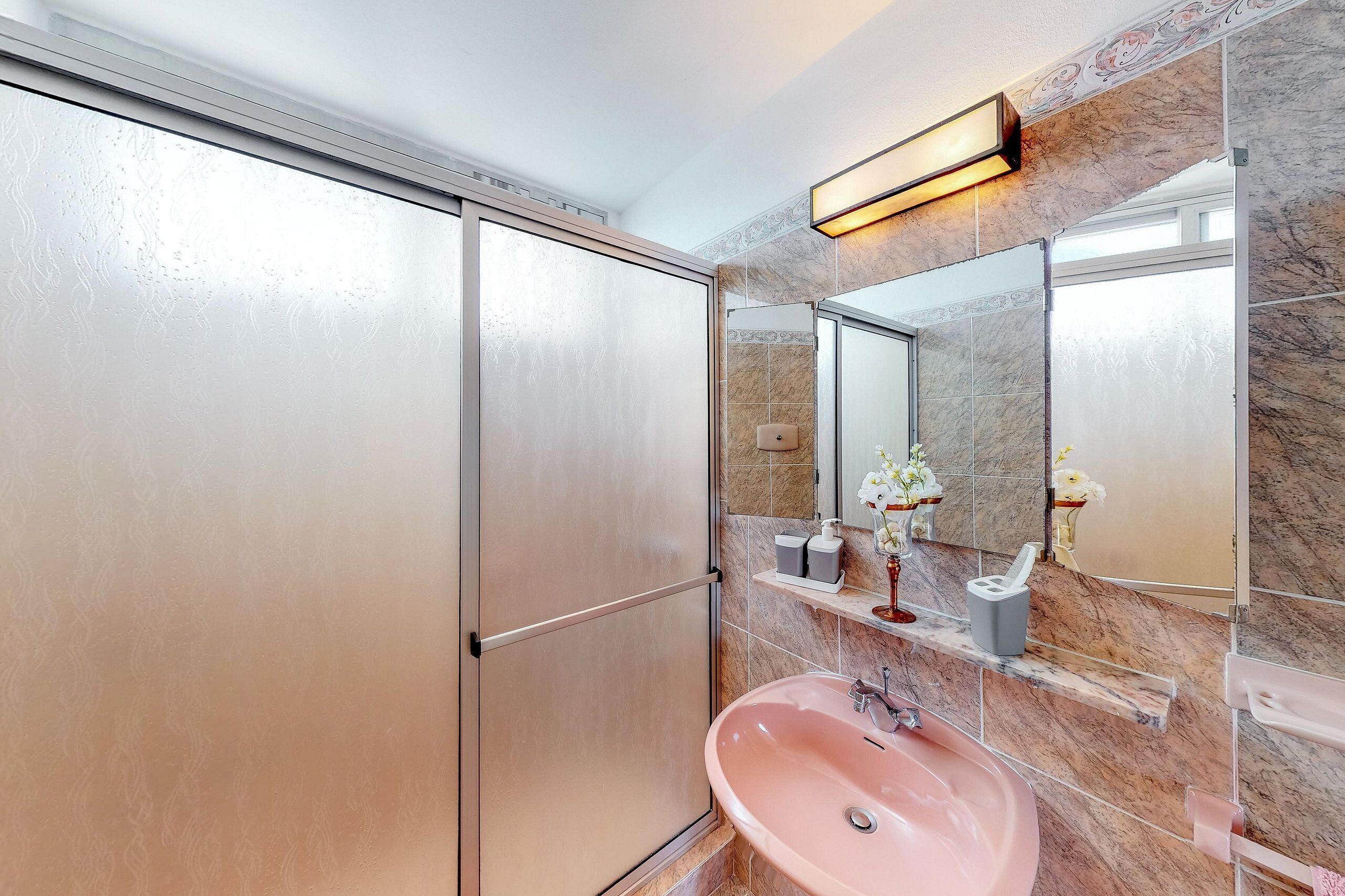 A bathroom with a pink sink, a mirror, and a shower enclosure.