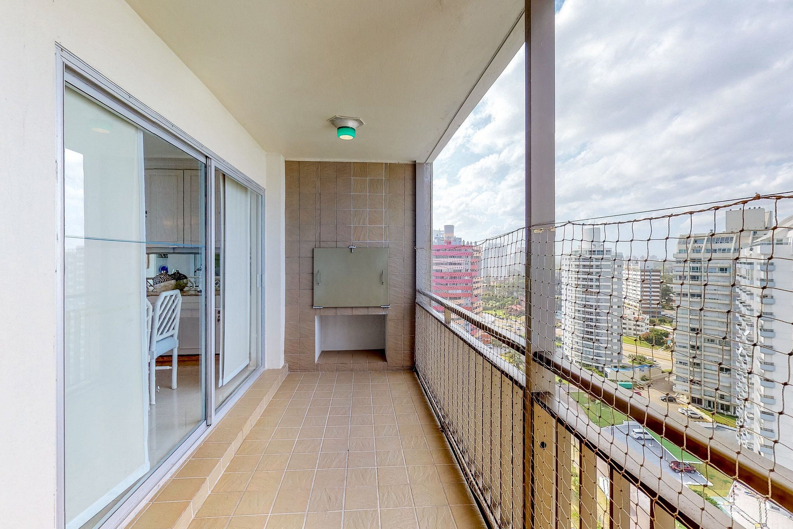 A balcony with a view of a cityscape, a glass door, and a tiled floor.