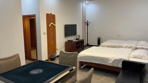 Quarto de hotel com cama, escrivaninha com computador, televisão e cabideiro.
