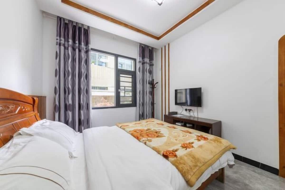 A bedroom with a bed, a TV, a window with curtains, and a view of buildings outside.