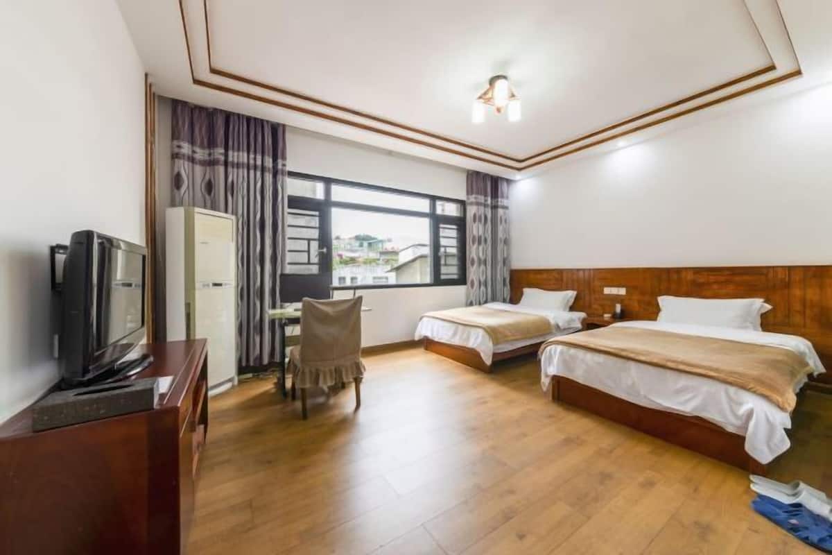 A hotel room with two beds, a desk, a television, and a window with curtains.