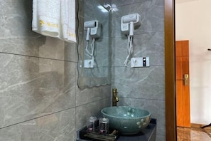 A bathroom with a marble wall, a large sink with a floral bowl, two hair dryers mounted on the wall, and a towel rack with towels. - Happy Heart Inn (Dafang)