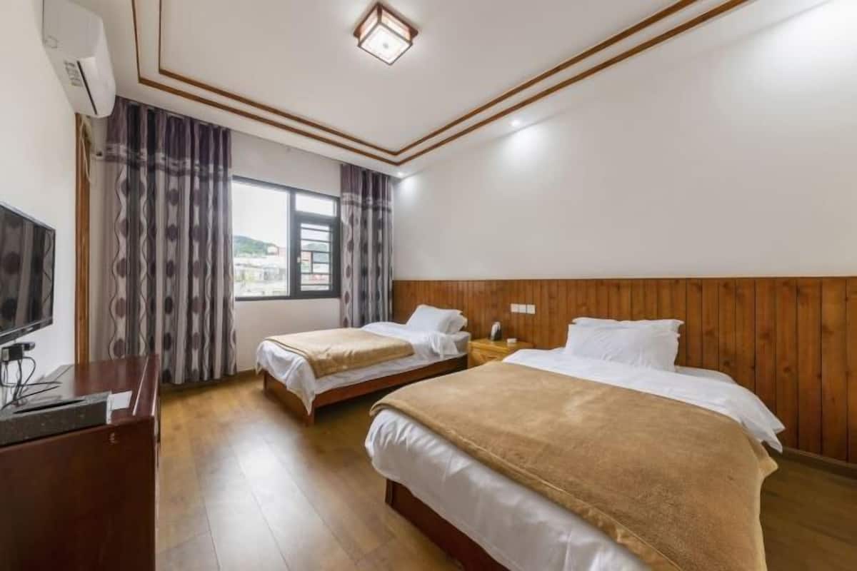 A hotel room with two beds, wooden paneling, a desk with a computer, and a window with curtains.