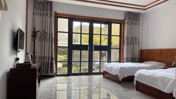 Quarto de hotel com duas camas, televisão, escrivaninha e grande porta de vidro corrediça para o exterior.