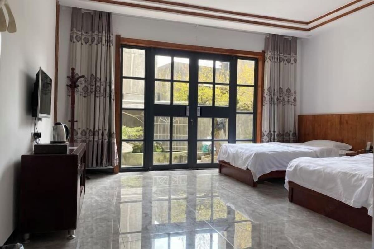 A hotel room with two beds, a TV, a desk, and a large sliding glass door to the outside.