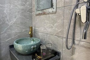 A bathroom with a stone sink, a handheld showerhead, and a small shelf with toiletries. - Happy Heart Inn (Dafang)
